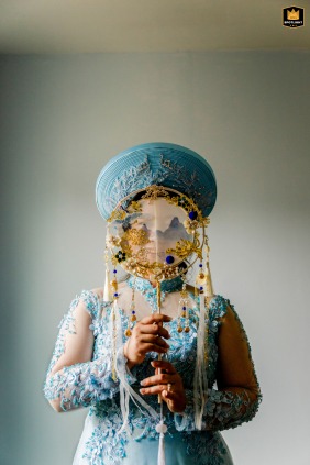 At the Church of Love in Maryland, the bride poses for a portrait holding a traditional cultural fan apparatus that covers her face, obscuring her expression.